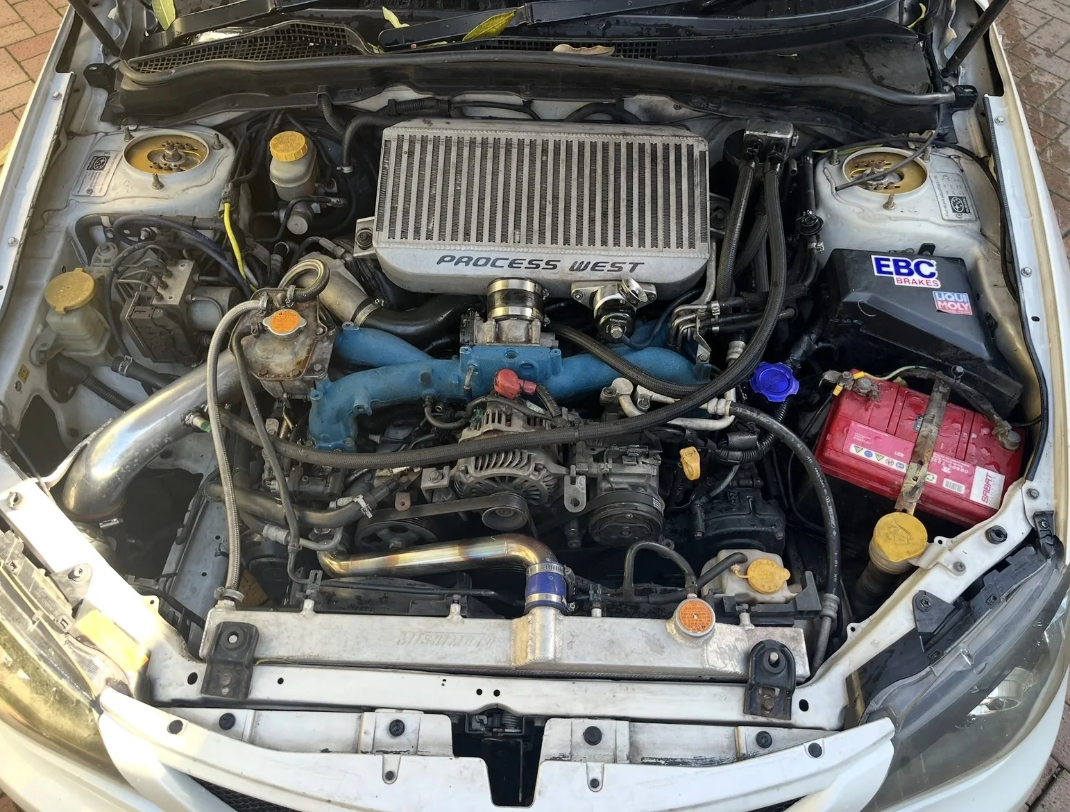 Subaru engine bay with blue intake components, polished pipework and a Process West intercooler